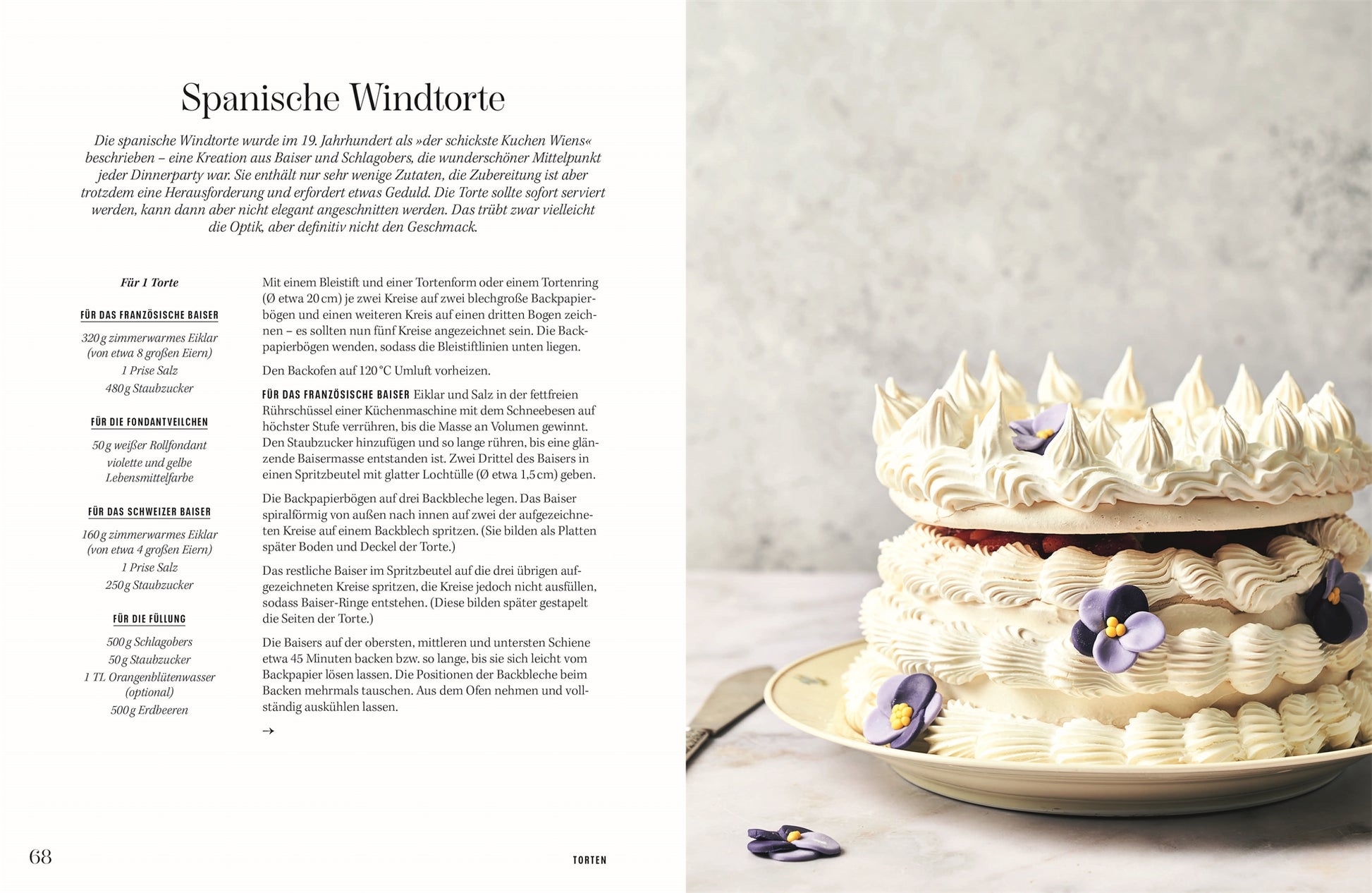 Rezept Spanische Windtorte: Große, kunstvoll verzierte Spanische Windtorte aus Baiser und Schlagobers, geschichtet mit dekorativen Tuffs und essbaren Blüten auf einer hellen Platte.