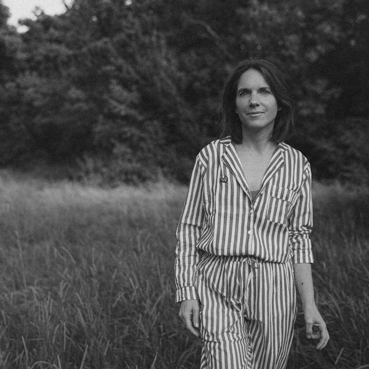 Porträtfoto von Bernadette Wörndl. Die Köchin, Food-Stylistin und Autorin steht in einem Feld und trägt ein gestreiftes Outfit. Das Schwarz-Weiß-Foto zeigt sie in natürlicher Umgebung und ruhiger, gelassener Haltung.