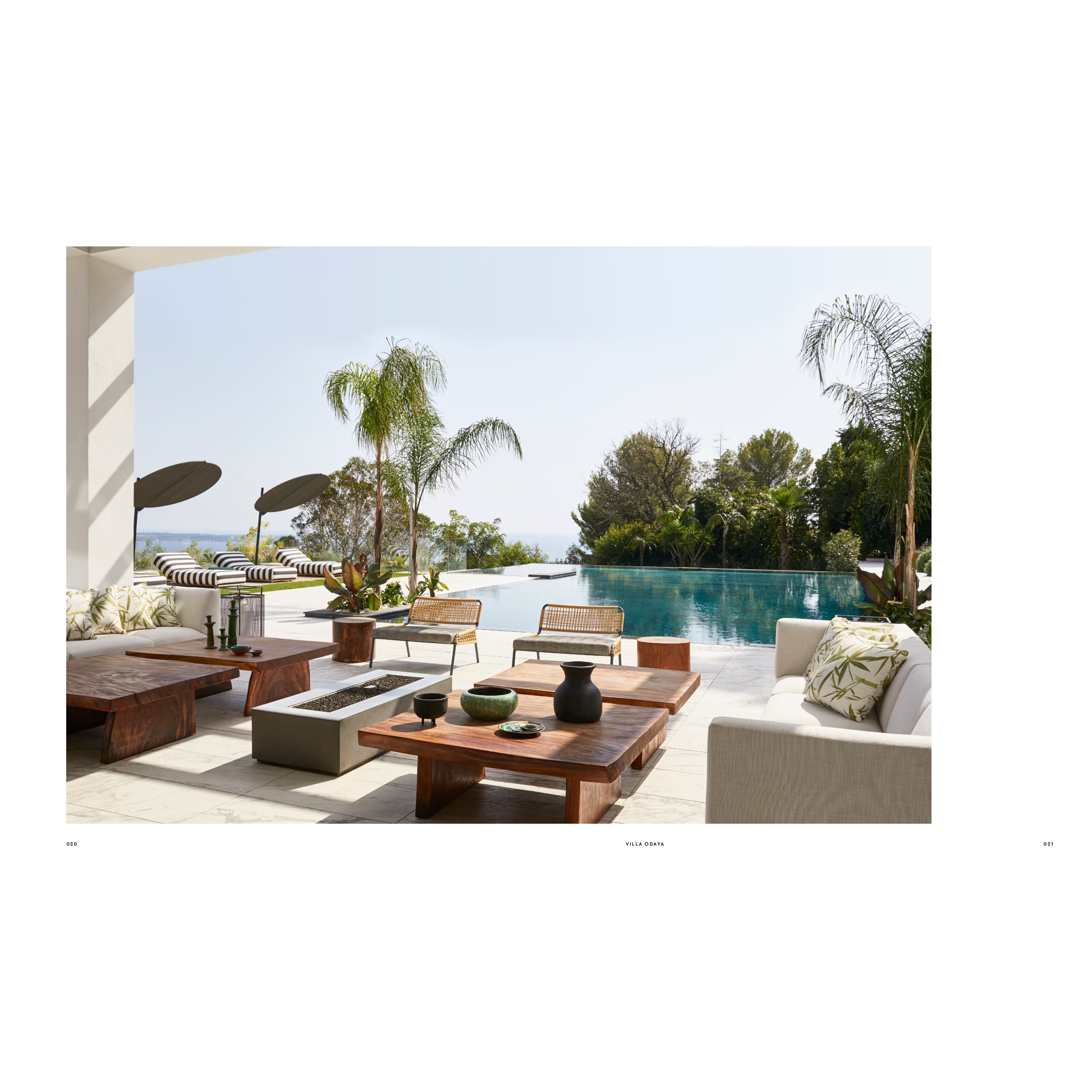 Luxuriöse Terrasse einer mediterranen Villa mit Infinity-Pool, Design-Holztischen, Rattanmöbeln und Palmenblick. Outdoor Living im modernen Côte-d’Azur-Stil.