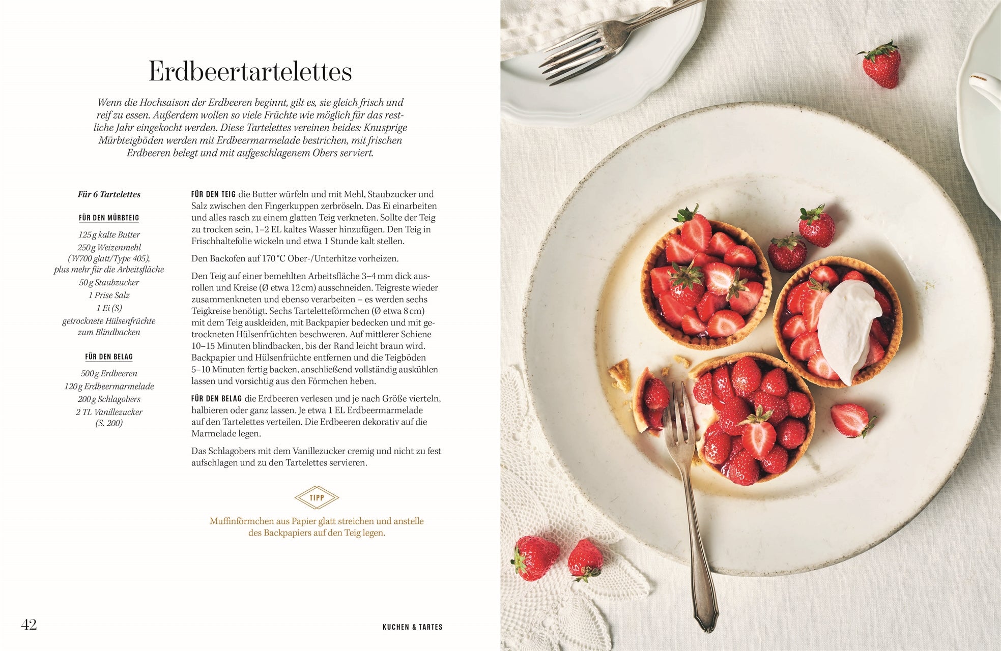 Erdbeertartelettes: Drei kleine Erdbeertartelettes auf einem weißen Teller, garniert mit frischen Erdbeeren und einem Klecks Schlagobers, daneben verstreut einige ganze Erdbeeren.