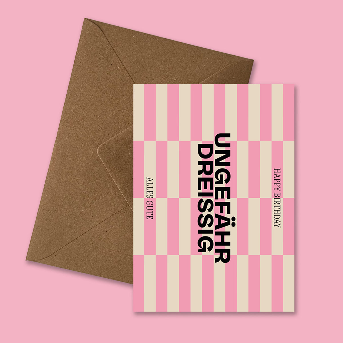 Moderne Geburtstagskarte ‚Ungefähr Dreissig‘ mit grafischem Streifenmuster in Pink und Beige, schwarzer Typografie und Aufschrift ‚Happy Birthday‘ und ‚Alles Gute‘, präsentiert mit braunem recyceltem Kraftpapier-Umschlag produziert in Deutschland