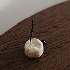 Minimalist ceramic incense holder in the shape of a face with a burning incense stick on a wooden table. Handcrafted design object made of cream colored glaze with dark speckles created for peaceful moments and modern interiors.