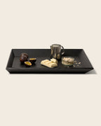 Schwarzes Holztablett OBLIQUE von NIEVEN mit schrägen Kanten. Darauf arrangiert: Passionsfrüchte, weiße Schokolade, eine Milchkanne und ein Glas Haferflocken. Modernes, minimalistisches Serviertablett im architektonischen Design von Jörg Adam.
