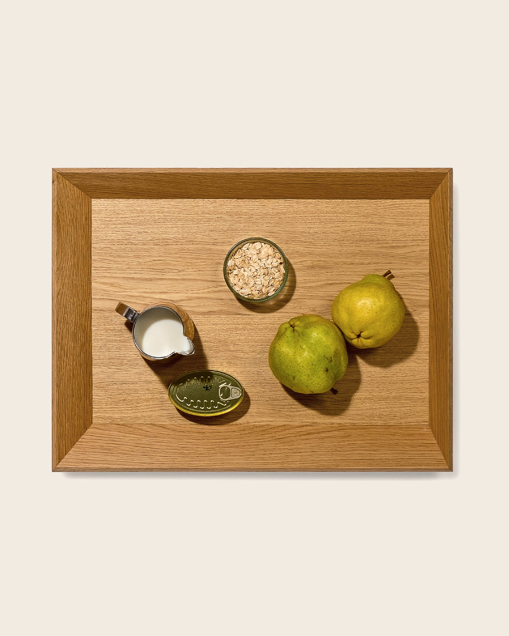 Holztablett OBLIQUE von NIEVEN mit architektonischem Design. Rechteckiges Eichenholz-Tablett mit abgeschrägten Kanten, auf dem Milch, Haferflocken, eine Dose und zwei Quitten arrangiert sind. Design von Jörg Adam.