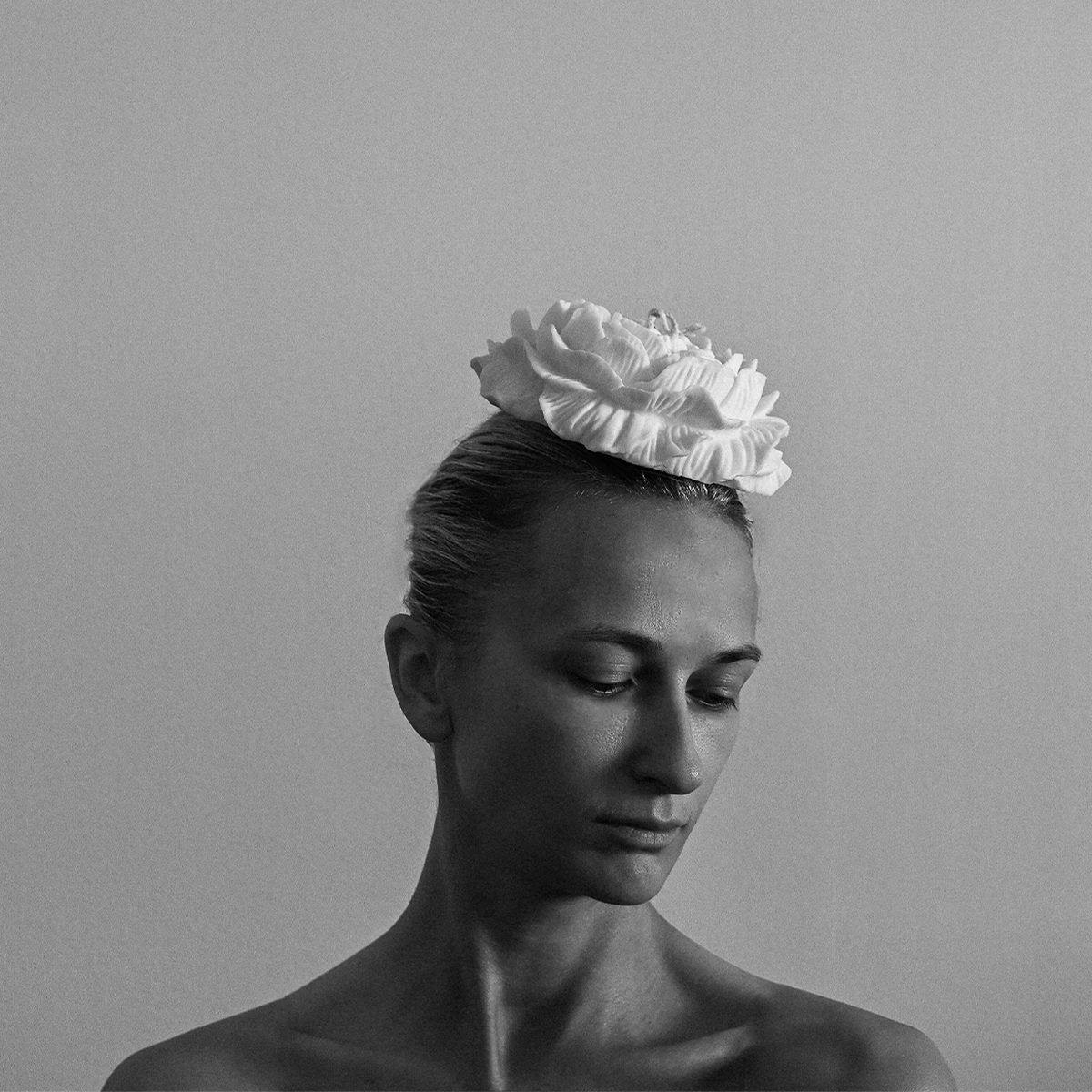 Porträtfoto von Olga Makinze, Gründerin von Studio ÜM. Die Kunsthandwerkerin blickt nach unten, trägt eine große, blütenförmige Kopfbedeckung und steht vor einem schlichten Hintergrund. Schwarz-Weiß-Aufnahme.