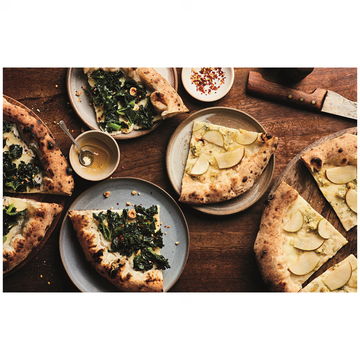 Verschiedene neapolitanische Pizzastücke mit luftigem Rand, belegt mit Blattgemüse, Käse und Birne, angerichtet auf Keramiktellern auf Holztisch