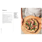 Kochbuch „Pizza Napoli-Style“: Pizza „Primavera“ mit luftigem Rand, belegt mit Schinken, Rucola und Kirschtomaten, serviert auf einem Holzbrett