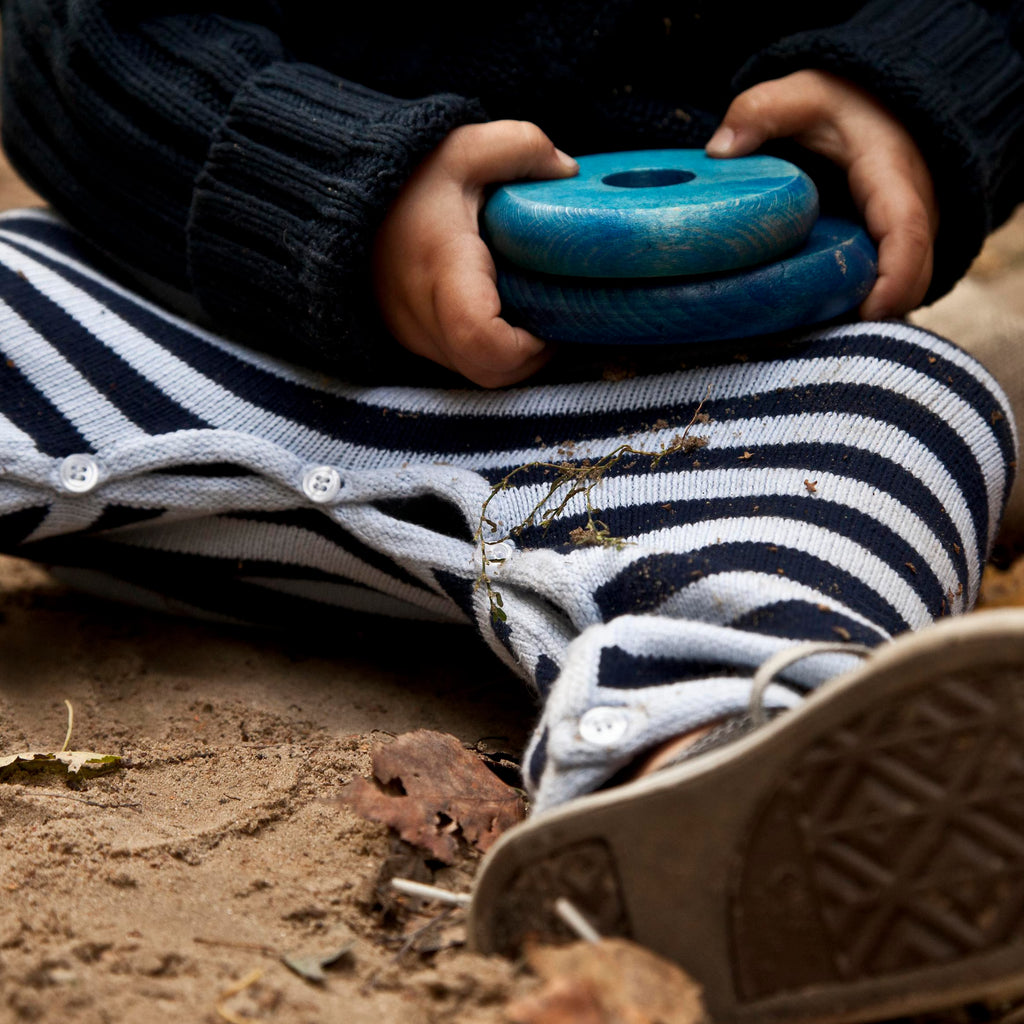 Detailaufnahme eines Kindes, das blaue Holzscheiben des Regenbogen Stapelturms in den Händen hält, hochwertiges Montessori Holzspielzeug aus Naturholz