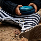 Detailaufnahme eines Kindes, das blaue Holzscheiben des Regenbogen Stapelturms in den Händen hält, hochwertiges Montessori Holzspielzeug aus Naturholz