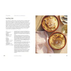 Natillas (Pudding mit Keks und Zimt): Zwei Tonförmchen mit cremigem Vanillepudding (Natillas), in der Mitte jeweils ein goldbraun gebackener Keks, bestreut mit Zimt und gehackten Mandeln. Daneben ein Glas Weißwein und eine Serviette.