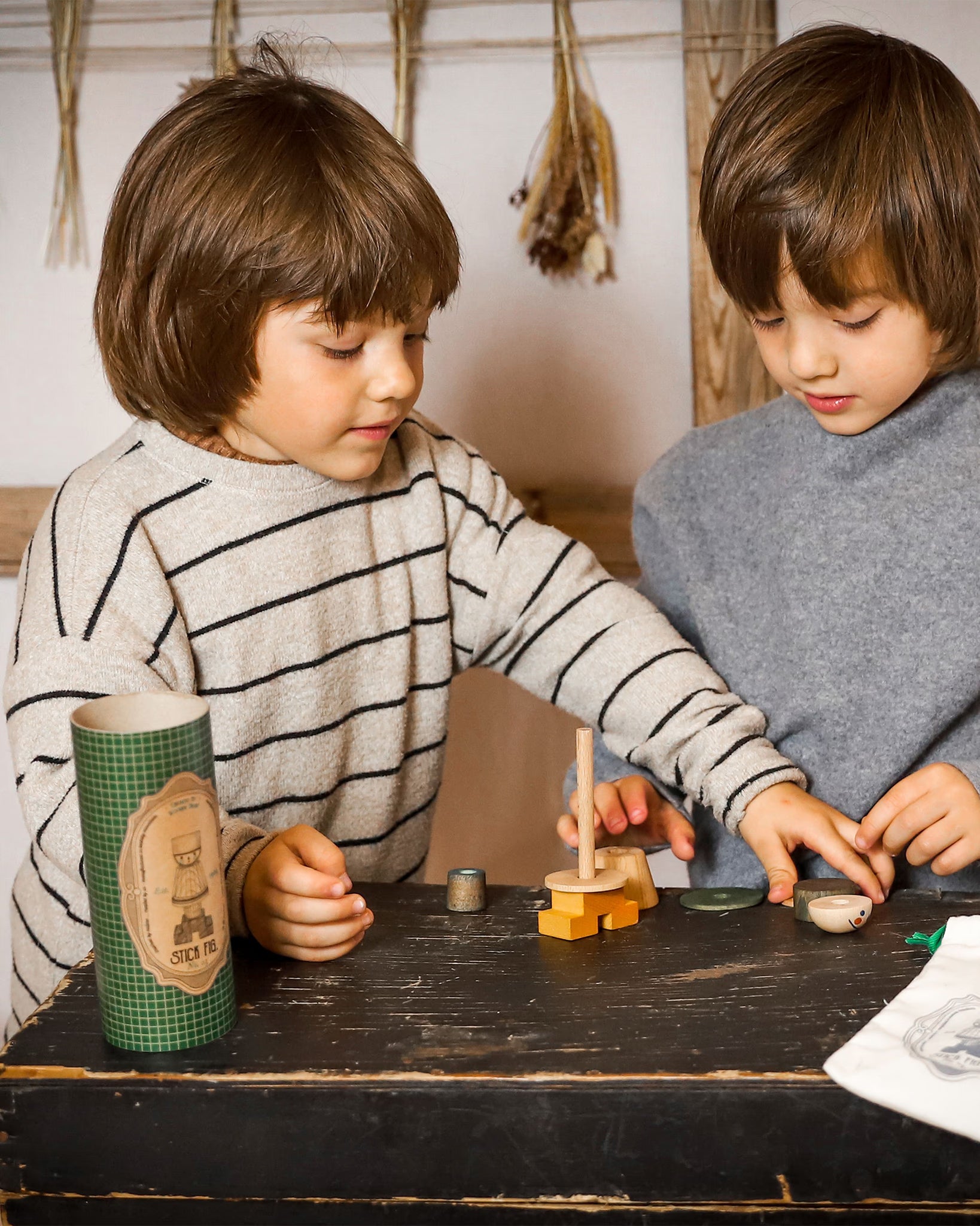 Zwei Kinder spielen gemeinsam mit einem Montessori-Holzsteckspiel aus naturbelassenem Holz an einem Tisch
