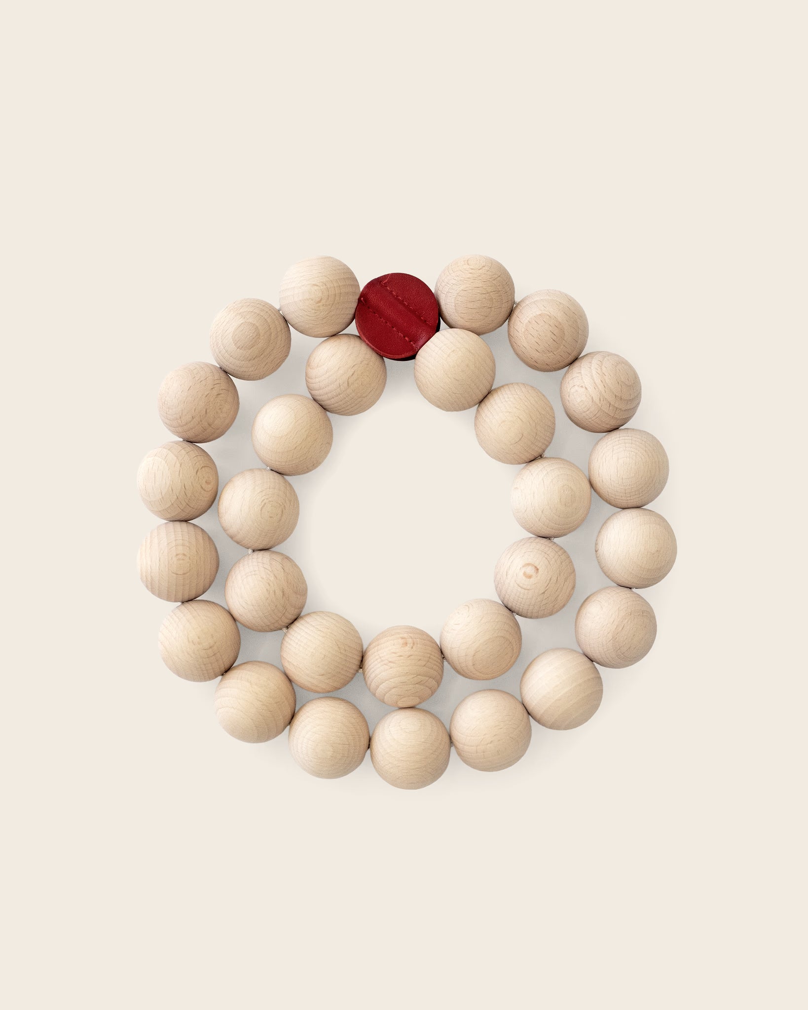 Topfuntersetzer PERLE von Siebensachen aus naturbelassenen Buchenholzkugeln mit zwei roten Lederpatches. Flexibel formbar als Kreis, Schleife oder Acht – stilvoller Schutz für Tisch und Holzoberflächen.