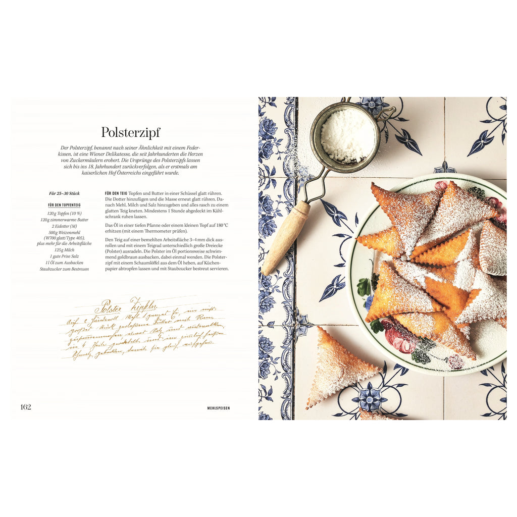 Rezept Polsterzipf: Goldbraun frittierte Polsterzipf-Dreiecke auf einem Teller, dick mit Staubzucker bestreut, daneben ein Sieb mit Puderzucker auf blauer, floral gemusterter Keramikplatte.