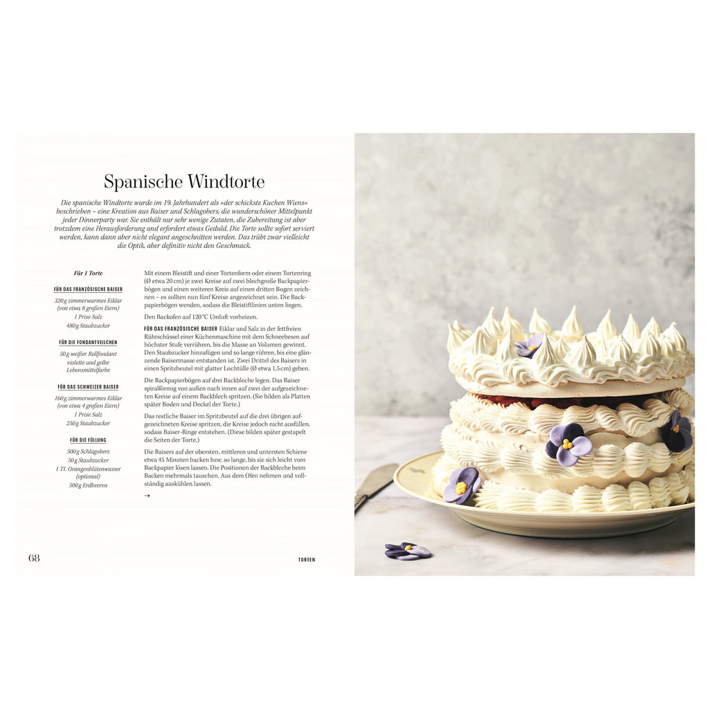 Rezept Spanische Windtorte: Große, kunstvoll verzierte Spanische Windtorte aus Baiser und Schlagobers, geschichtet mit dekorativen Tuffs und essbaren Blüten auf einer hellen Platte.