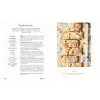 Rezept Topfenstrudel: Frisch gebackener Topfenstrudel auf Backpapier, in Stücke geschnitten, mit Staubzucker bestäubt; rustikale Optik auf gefliester Unterlage.