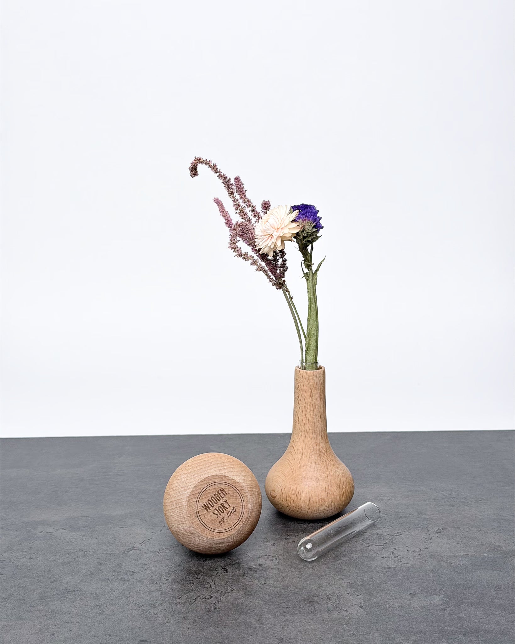 Zwei Holzvasen Kropla von Wooden Story mit Trockenblumen. Logo von Wooden Story auf dem Boden. Danaben das Reagenzglass liegend.