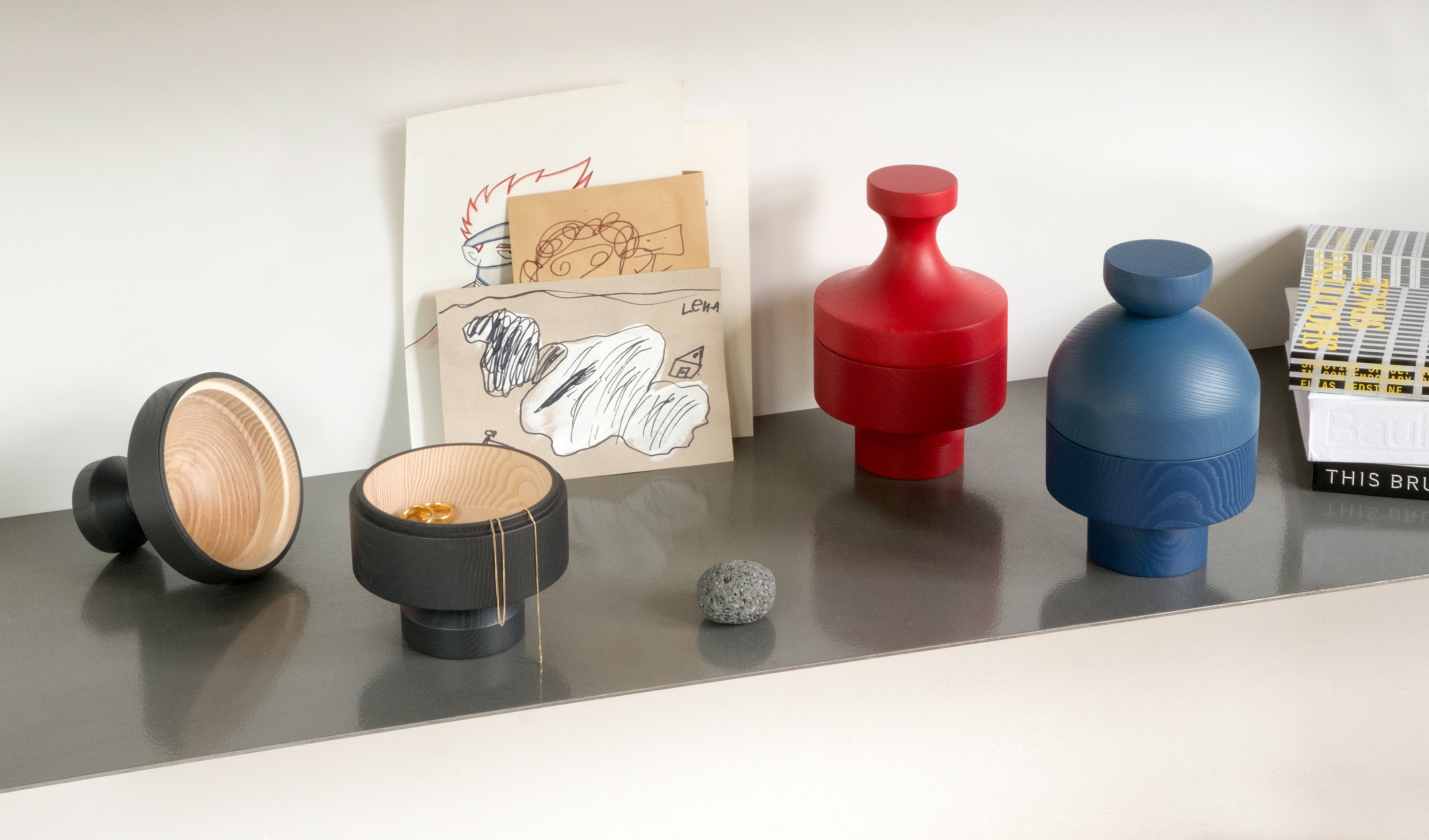 Design objects ANUKI HINTO and DEVAKI by NIEVEN displayed on a shelf in red blue and black hand-turned ash wood bowls modern home accessories for storage and decoration made in Germany.