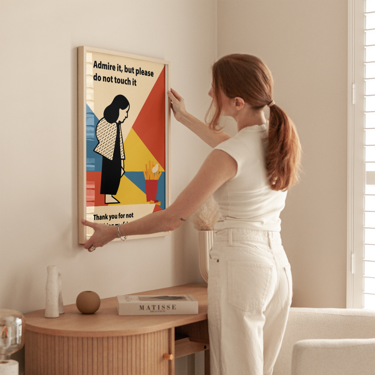Frau hängt Fine Art Print Admire it but please do not touch it von mikkaneo studio im Wohnzimmer auf. Moderner Kunstdruck in kräftigen Farben mit Retro Stil, im Bauhaus Stil.