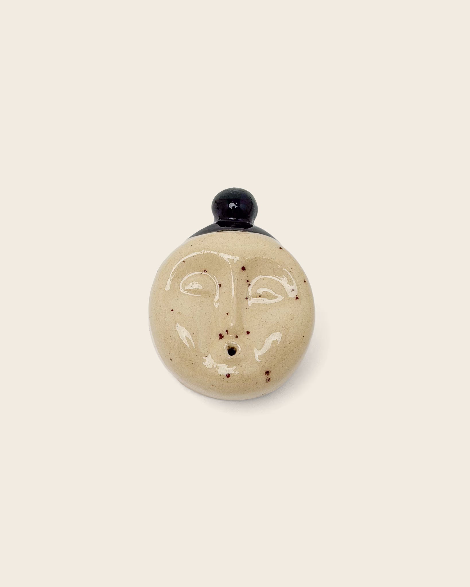 Handgefertigter Keramik-Räucherstäbchenhalter in Gesichtsform mit cremefarbener Glasur und dunklen Sprenkeln, minimalistisches Designobjekt mit schwarzer Kappe. Stilvolle Keramikdekoration für modernes Wohnen.