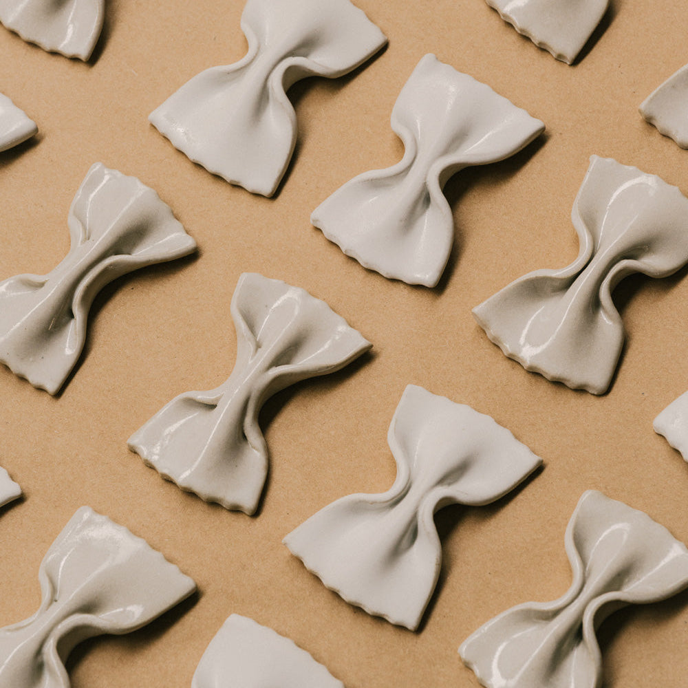 Mehrere handgefertigte LA FARFALLE Messerablagen aus Keramik von OEUVRES SENSIBLES auf braunem Untergrund. Inspiriert von italienischer Farfalle-Pasta, glänzende Glasur in Farbe Grès Shinny, gefertigt in Marseille. Stilvolle Tischaccessoires aus Frankreich. Bild © Maxime Verret