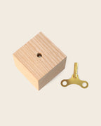 Spieluhr ‚Nature Spring‘ von Siebensachen: naturbelassener Eschenholz-Block mit sichtbarer Aufzugsöffnung und goldenem Aufziehschlüssel aus Metall.