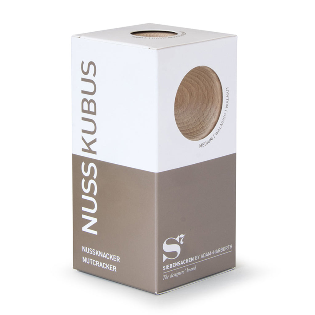 Verpackung des Nussknackers NUSSKUBUS von Siebensachen mit Sichtfenster, das das Buchenholz zeigt. Hochwertige Box in Weiß und Braun mit modernem Design und klarer Typografie.