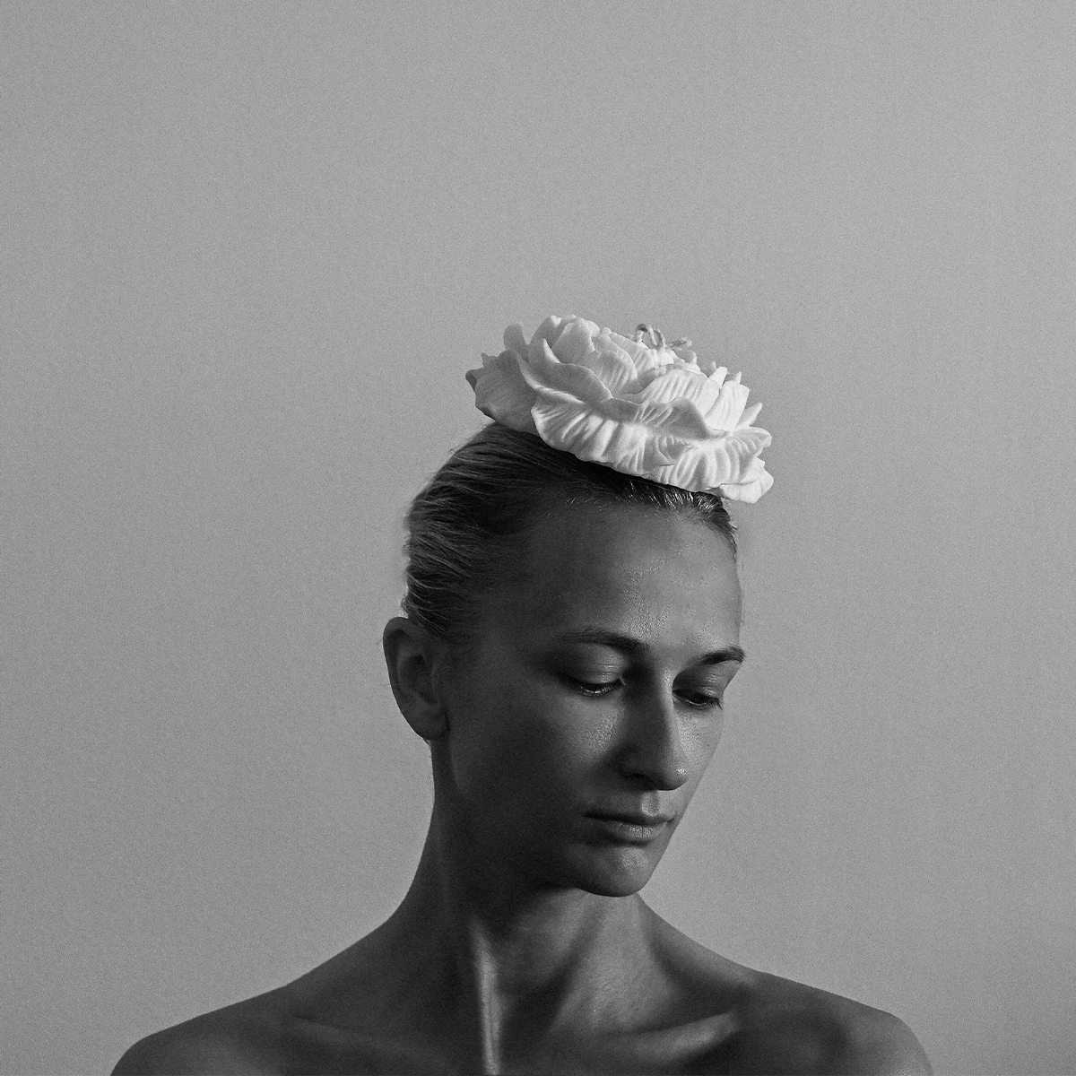 Porträtfoto von Olga Makinze, Gründerin von Studio ÜM. Die Kunsthandwerkerin blickt nach unten, trägt eine große, blütenförmige Kopfbedeckung und steht vor einem schlichten Hintergrund. Schwarz-Weiß-Aufnahme.