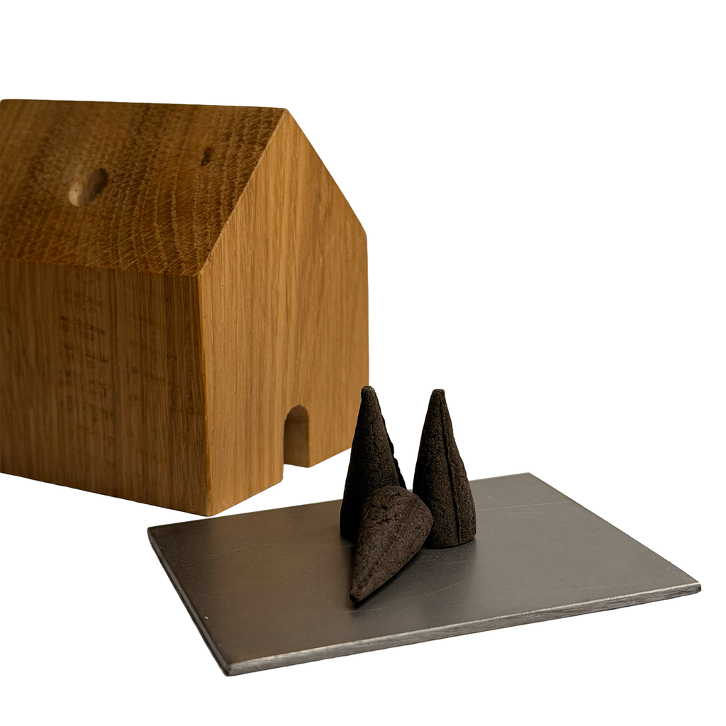 Holzräucherhäuschen aus recyceltem Eichenholz mit kleiner Türöffnung, daneben drei schwarze Räucherkegel auf einer Edelstahlplatte.