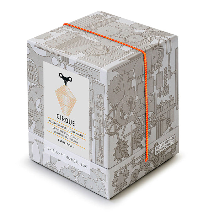 Spieluhr CIRQUE von Siebensachen in hochwertiger Geschenkbox mit grafischem Zahnraddesign und oranger Kordel. Handgefertigt im Schwarzwald aus Buche, spielt „Guten Abend, gut’ Nacht“.