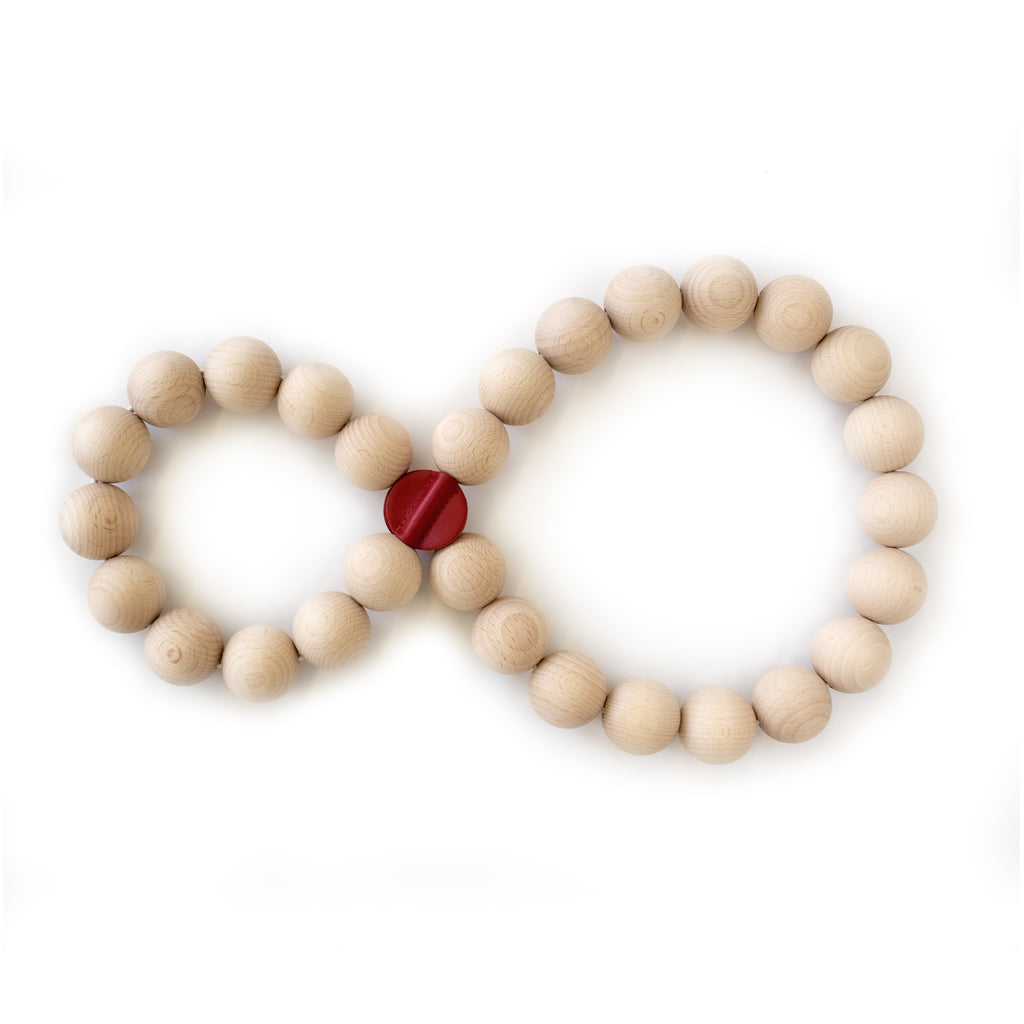 Topfuntersetzer PERLE von Siebensachen in Form einer Acht gelegt. Gefertigt aus naturbelassenen Buchenholzkugeln mit roten Lederpatches. Flexibel und dekorativ für mehrere Töpfe.