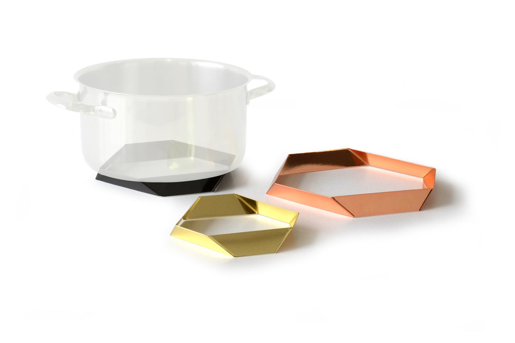 Design-Untersetzer-Set HEXAGON von Siebensachen aus polierten Metallbändern. Glänzt in den Farben Messing, Kupfer und Gold. Die prismatischen Elemente dienen als stilvolle Topfuntersetzer und lassen sich zu einer dekorativen Tischskulptur arrangieren. Teil der A+H Foreign Affairs Reihe.