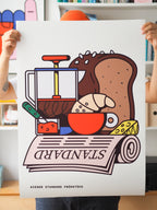 Fine Art Print Wiener Standard Frühstück by RadandYellow from Vienna held in hands showing a colorful illustration of a classic Viennese breakfast with croissant bread cheese jam coffee press and newspaper. The limited art print combines pop art with Austrian breakfast culture bringing playful lightness to modern living spaces.